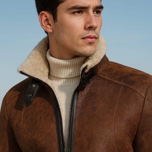 May include: A brown leather jacket with a cream-colored shearling collar and a matching turtleneck sweater. The jacket has a black zipper and black leather accents. The background is a light blue.