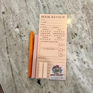 以下が含まれることがあります： タイトル、著者、プロットのプロンプトが付いた、桃色の本のレビューメモ帳。オレンジ色のペン、ピンク色のペン、桃色の付箋2枚も含まれています。「BOOKTROVERT」という言葉と花が描かれたステッカーもあります。