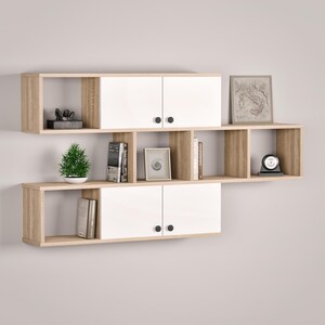 May include: A modern wall-mounted shelving unit with a combination of light wood and white cabinets. The unit features open shelves, closed cabinets with black knobs, and is decorated with books, a small plant, and decorative items.