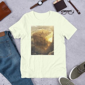 Op de afbeelding: Lichtgeel T-shirt met een afbeelding van een gouden kubus en de tekst "Biblically Accurate". De afbeelding bevat gedetailleerde beelden en tekst eronder. Het shirt is gemaakt van zacht materiaal.