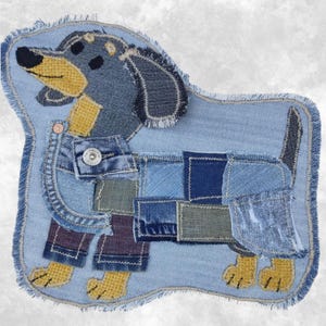 Pode incluir: Um emblema de tecido em forma de cão dachshund, feito com vários tons de ganga azul e tecido amarelo. O design apresenta uma borda desfiada, um detalhe de botão de metal prateado na área do peito e detalhes em tecido roxo nas pernas.