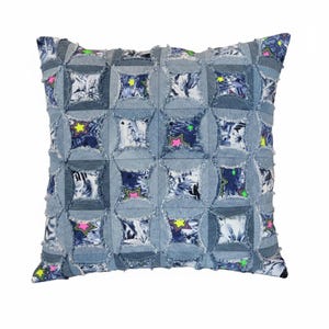 Puede incluir: Cojín cuadrado de mezclilla con diseño de patchwork. El cojín presenta una base de mezclilla azul claro con un patrón de cuadrados. Cada cuadrado contiene un estampado floral y una estrella con acentos rosa neón y amarillo. Los bordes de la mezclilla están deshilachados.