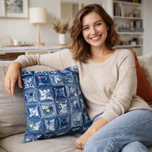 May include: A square denim pillow with a patchwork design. The pillow features a pattern of blue denim squares and circles, with colorful floral and star accents. The pillow is on a neutral-colored sofa.