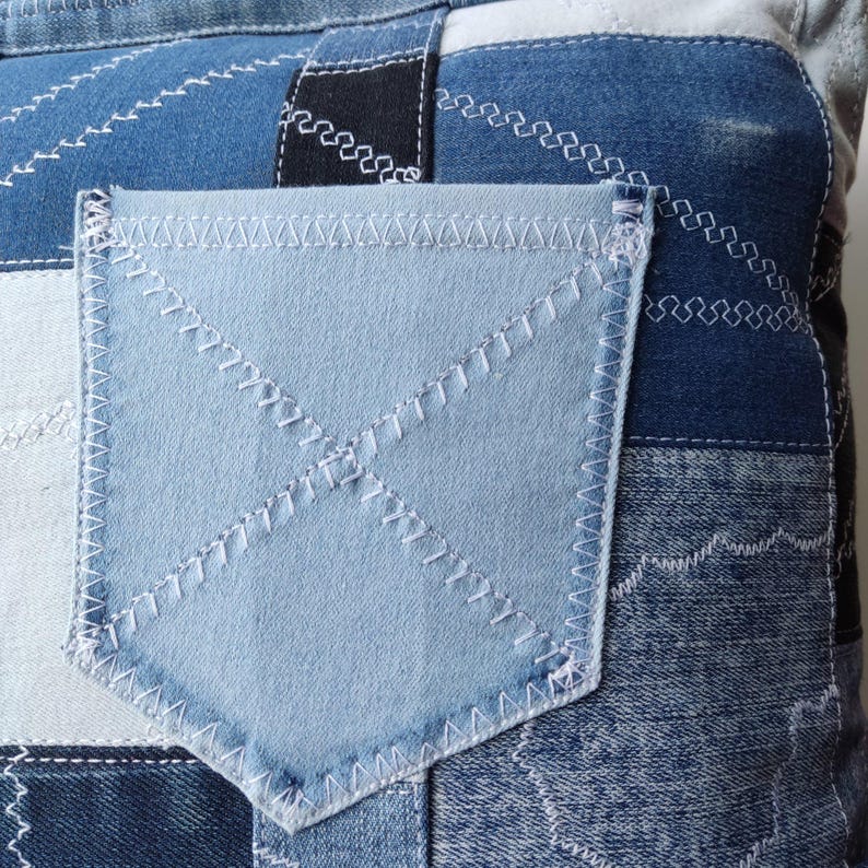 Pu&ograve; includere: Primo piano di un tessuto denim patchwork con una tasca azzurra. Il denim presenta varie tonalit&agrave; di blu, con dettagli di cucitura bianchi. La tasca &egrave; di una tonalit&agrave; di blu pi&ugrave; chiara ed &egrave; cucita con filo bianco.