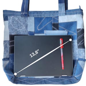 Pu&ograve; includere: Una borsa tote in denim patchwork con un laptop nero all'interno. Il laptop misura 35 cm in diagonale. Una penna rossa &egrave; appoggiata sul laptop. La borsa &egrave; realizzata in denim blu di varie tonalit&agrave; e ha una piccola tasca.