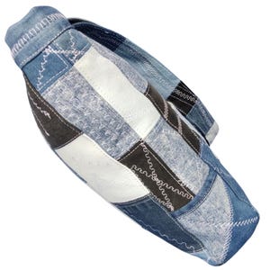 Pu&ograve; includere: Borsa a tracolla in denim patchwork nei toni del blu, bianco e nero. I pannelli della borsa sono cuciti insieme con filo bianco. La borsa ha una forma curva e una tracolla, offrendo un'estetica unica e artigianale.
