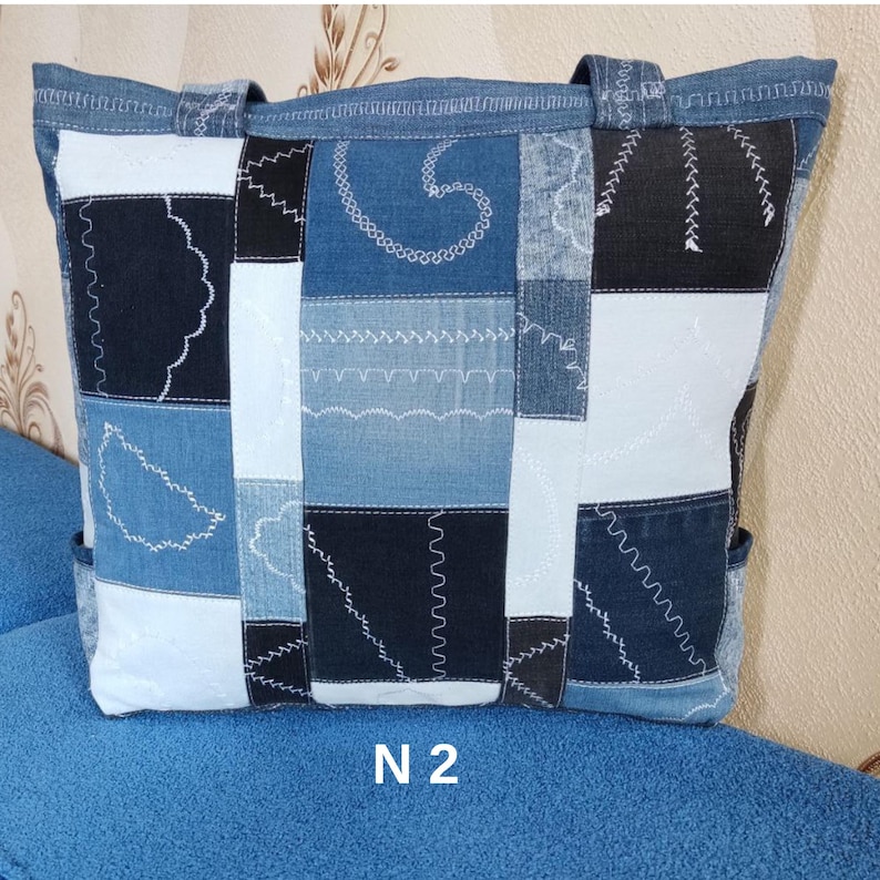 Pu&ograve; includere: Una borsa tote in denim con un design patchwork. La borsa presenta quadrati di denim blu di diverse tonalit&agrave;, cuciti insieme con filo bianco. Ha due manici e il testo "N 2" &egrave; visibile in basso.