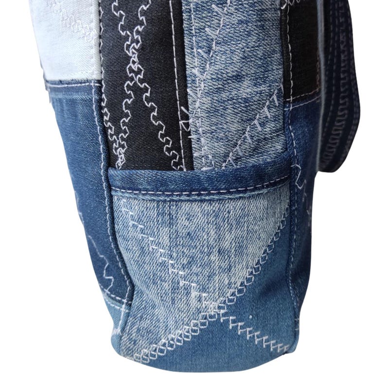 Pu&ograve; includere: Una borsa tote in denim patchwork con una tasca. La borsa presenta varie tonalit&agrave; di denim blu, tessuto nero con cuciture bianche e dettagli di cuciture bianche. Il design della borsa &egrave; un mix di forme e motivi geometrici.