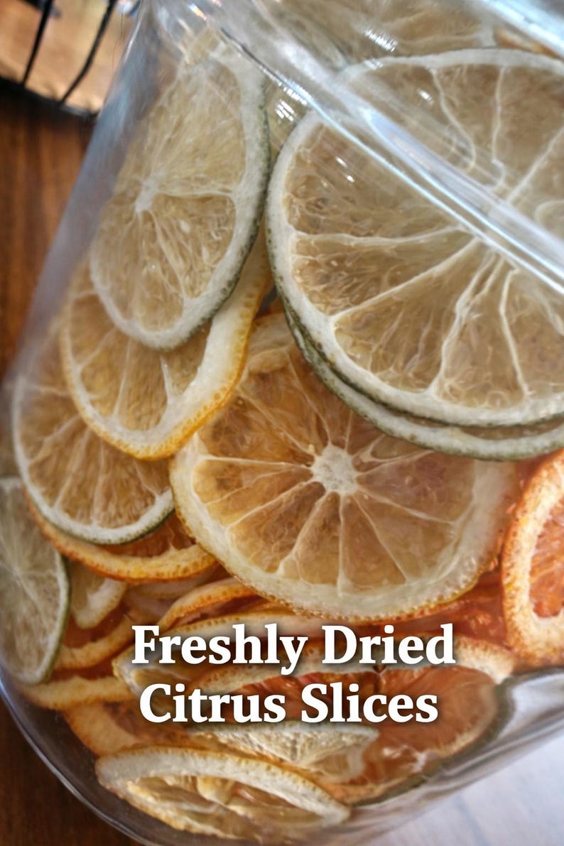 May include: A clear glass jar filled with freshly dried citrus slices. The slices are a mix of oranges, lemons, and limes, with a variety of colors from light yellow to deep orange. Text on the jar reads "Freshly Dried Citrus Slices."