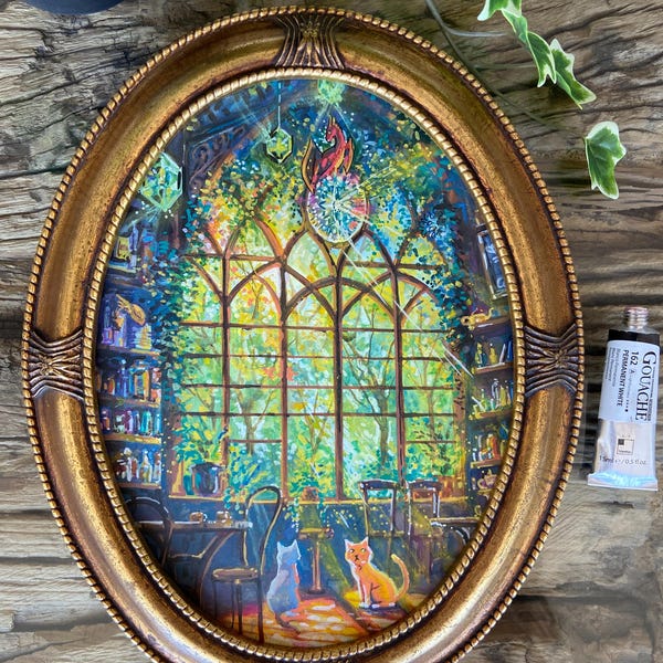 May include: Oval, gold-framed painting showing a fantastical interior with a large window looking onto a vibrant garden. Two cats are on the floor. A gouache paint tube is visible. The painting is on a wooden surface.