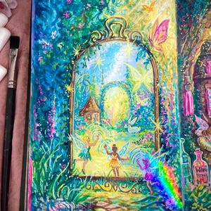 May include: A colourful illustration in an open book, showing a magical garden scene. The artwork features fairies, butterflies, and a small house within a decorative arch, surrounded by lush greenery and a rainbow.