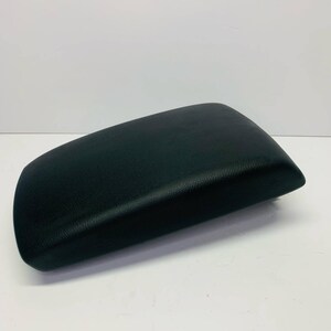 May include: A black, rectangular car armrest with a textured finish. The armrest has a gently curved shape and is likely made from a robust material. It is shown against a white backdrop.