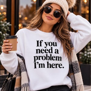 Puede incluir: Una sudadera blanca de manga larga con cuello redondo que presenta el texto impreso en negro If you need a problem I'm here. La prenda tiene un corte estándar con puños y cuello acanalados, ofreciendo un aspecto limpio y sencillo.
