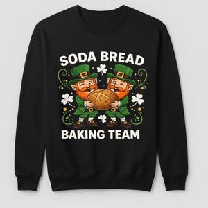 Puede incluir: Sudadera negra con un gráfico de dos duendes sosteniendo una hogaza de pan. El texto "SODA BREAD BAKING TEAM" está impreso arriba y abajo de la ilustración. Los duendes visten trajes y sombreros verdes.