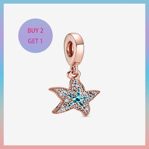May include: A rose gold starfish charm with a loop for a bracelet or necklace. The starfish is encrusted with small, light blue and clear crystals. The image also includes a purple circle with the text "BUY 2 GET 1".