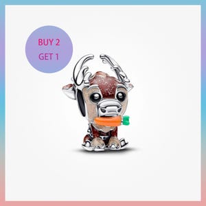 Könnte beinhalten: Ein silberfarbener Charm, der ein sitzendes Rentier mit großen Augen, Geweih und einer Karotte im Mund darstellt. Der Charm hat braune und beige Akzente. Ein lila Kreis mit dem Text "BUY 2 GET 1" befindet sich im Hintergrund.