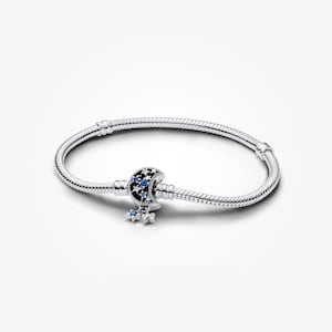 May include: A silver bracelet with a moon and star charm. The charm features a crescent moon design with blue accents and dangling stars. The bracelet is made of a flexible, snake-like chain.