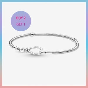 May include: A silver snake chain bracelet featuring a looped infinity-style clasp mechanism. The bracelet has two fixed stations along the chain and a circular purple graphic in the upper left corner with the text BUY 2 GET 1 in pink letters.