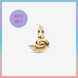 May include: A gold-colored charm in the shape of a nautilus shell, with a loop for attaching to a bracelet or necklace. The charm has star-shaped accents and the text "BUY 2 GET 1" in a purple circle.