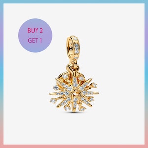 Puede incluir: Un charm dorado con un diseño de estrella, adornado con numerosos cristales transparentes. El charm tiene un lazo para sujetarlo y está sobre un fondo degradado. El texto "BUY 2 GET 1" está en un círculo morado.