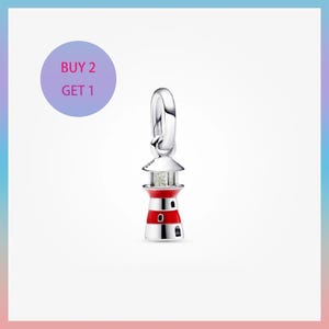 Può includere: Un charm a forma di faro argentato con dettagli in smalto rosso e bianco. Il charm presenta un piccolo anello per l'attacco e un design dettagliato del faro. L'immagine include anche un cerchio viola con il testo "BUY 2 GET 1".