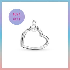 Può includere: Un charm a forma di cuore argentato con un design strutturato. Il charm ha un piccolo anello nella parte superiore e una perla rotonda con la scritta "PANDORA". L'immagine include anche un cerchio viola con il testo "BUY 2 GET 1".
