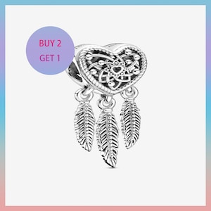 May include: A silver charm featuring a heart-shaped top and three feather pendants. The heart has an intricate pattern with a central heart motif. The image includes a purple circle with the text "BUY 2 GET 1".
