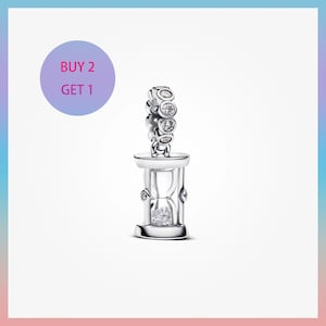May include: A silver-colored charm in the shape of an hourglass, with a sparkling gem-filled center and a loop adorned with clear stones. The charm is displayed against a white background with a purple circle that says "BUY 2 GET 1".