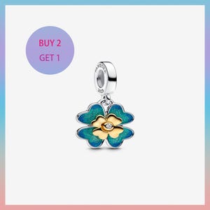Puede incluir: Un charm de plata con un diseño de trébol de cuatro hojas. El trébol tiene esmalte turquesa y dorado con un pequeño diamante en el centro. El charm está suspendido de un lazo plateado con el nombre de la marca y la fecha.