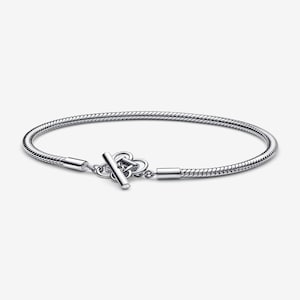 May include: A silver-colored bracelet with a snake chain design. The bracelet features a toggle clasp with a decorative heart-shaped element. The bracelet is a simple, elegant piece of jewelry.