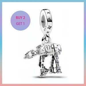 May include: A silver charm depicting an AT-AT walker from Star Wars. The charm has intricate detailing and a loop at the top for attaching to a bracelet or necklace. The charm is shown against a white background with a purple circle that says "BUY 2 GET 1".