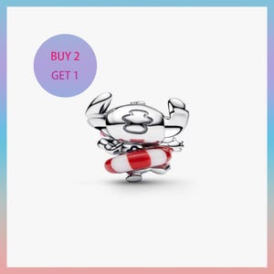 May include: A silver charm depicting the character Stitch from Lilo & Stitch, wearing a red and white striped life preserver. The charm has a polished finish and is set against a gradient background. A purple circle with the text "BUY 2 GET 1" is in the upper left.