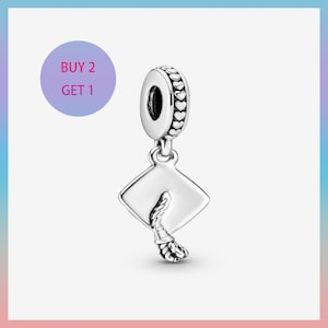 May include: A silver-colored graduation cap charm with a tassel. The charm has a loop at the top with heart-shaped details. A purple circle with the text "BUY 2 GET 1" is in the background.