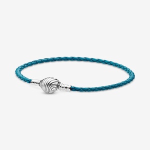 May include: A teal braided leather bracelet with a silver clasp. The clasp is a round, textured design. The bracelet is a simple, elegant accessory. The leather appears to be a vibrant shade of teal.