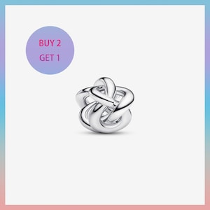 May include: A silver-colored charm with an intertwined knot design. The charm is made of a shiny metal and has a smooth, polished surface. A purple circle with the text "BUY 2 GET 1" is in the upper left corner.