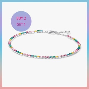 May include: A silver-tone tennis bracelet featuring a continuous row of small, round, multi-colored gemstones in shades of pink, yellow, green, and blue. The bracelet includes a lobster claw clasp and a small extender chain with text BUY 2 GET 1.