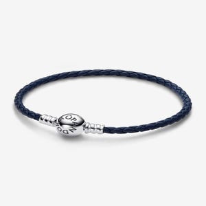 May include: A navy blue braided leather bracelet with a silver clasp. The clasp features the brand name. The bracelet is a simple, elegant accessory.