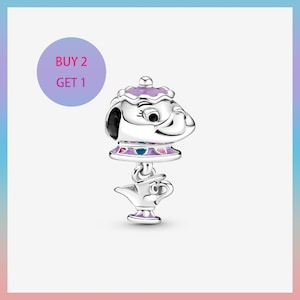 May include: A silver charm featuring a stylized teapot with a purple lid and a smaller teapot charm below. The charm has a whimsical design with black accents and colorful details. The text "BUY 2 GET 1" is in a purple circle.