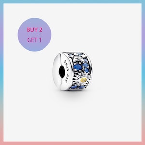 Può includere: Un charm in argento con un design celeste. Il charm presenta pietre preziose blu e trasparenti, con un motivo a sole e stella. Il testo "S925 ALE" è visibile sul lato. Un cerchio viola con il testo "BUY 2 GET 1" è sullo sfondo.