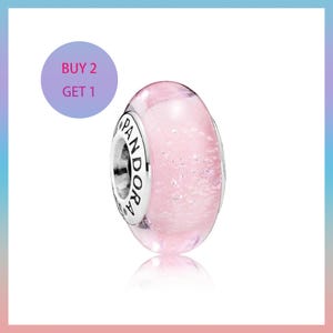 May include: A pink glass bead with silver accents and the word "PANDORA" engraved on the silver ring. The bead has a glittery, speckled appearance. A purple circle with the text "BUY 2 GET 1" is in the background.
