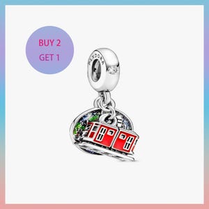 May include: A silver charm with a red train design. The charm has a round pendant with a detailed landscape and a red train. The charm has the word "Pandora" on the top. The text "BUY 2 GET 1" is in a purple circle.