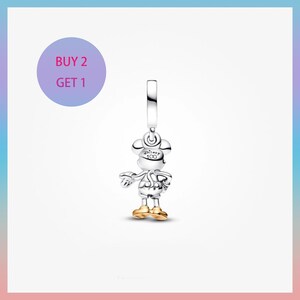 May include: A silver Mickey Mouse charm with gold-colored shoes and accents. The charm has a loop at the top for attachment and features the text "Disney 100". A purple circle with the text "BUY 2 GET 1" is in the upper left corner.