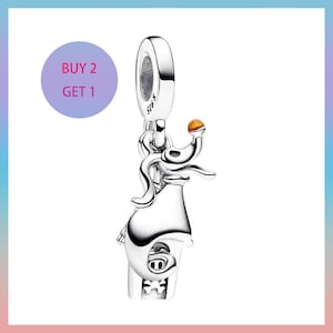 Puede incluir: Un charm de plata con un diseño de casa, con una pequeña gema naranja en la parte superior. El charm tiene un lazo para sujetarlo a una pulsera o collar. El texto "BUY 2 GET 1" está en un círculo morado en la esquina superior izquierda.