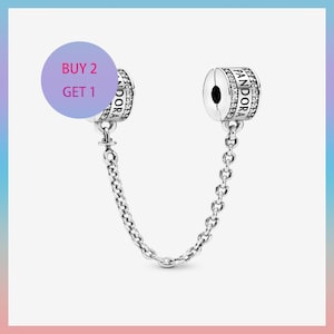 Może przedstawiać: Srebrny łańcuszek zabezpieczający Pandora z dwoma cylindrycznymi zawieszkami. Każda zawieszka ma logo Pandora i jest ozdobiona małymi, przezroczystymi kamieniami. Łańcuszek łączy dwie zawieszki. Fioletowe koło z napisem "BUY 2 GET 1".