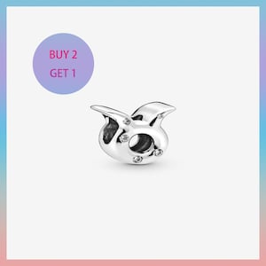 May include: A silver charm shaped like the Taurus zodiac symbol, adorned with small, clear gemstones. The charm has a polished finish and a circular opening. A purple circle with the text "BUY 2 GET 1" is in the upper left corner.