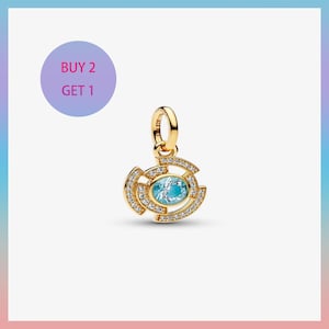 May include: A gold-colored pendant with a light blue oval gemstone at the center, surrounded by a spiral design encrusted with small, clear gemstones. The pendant has a loop at the top for attaching to a chain. The text "BUY 2 GET 1" is in a purple circle.