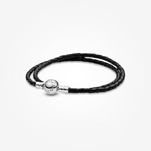 May include: A black leather double-wrap bracelet with a silver clasp. The bracelet features a braided design and a round clasp with engraved text. The jewelry is displayed on a white background.