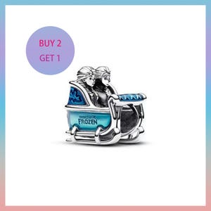 May include: A silver charm featuring two figures in a blue and silver carriage. The charm has the words "World of Frozen" on the front. A purple circle with the text "BUY 2 GET 1" is in the upper left corner.