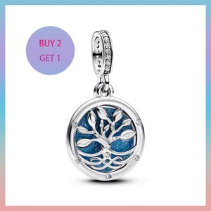Puede incluir: Colgante plateado con un diseño de árbol de la vida. El colgante presenta un centro redondo azul-verdoso con una silueta de árbol y detalles de cristal transparente. La fianza está incrustada con pequeños cristales transparentes. El texto "BUY 2 GET 1" está en un círculo morado.