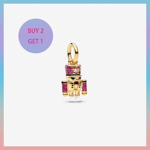 May include: Gold-toned charm in the shape of a toy soldier. The soldier has a red and glittery hat, red accents, and a star-shaped gem. The charm has a loop for attaching to a bracelet or necklace. The image also includes the text "BUY 2 GET 1".
